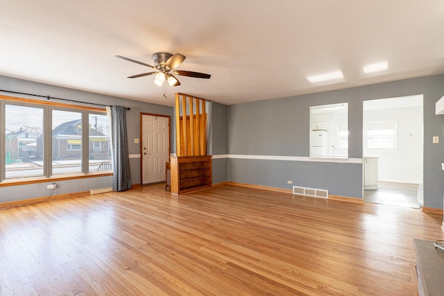 interior space featuring a ceiling fan, light wood-style flooring, visible vents, and baseboards