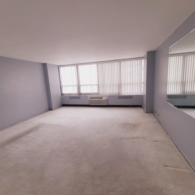 carpeted spare room featuring an AC wall unit and a healthy amount of sunlight