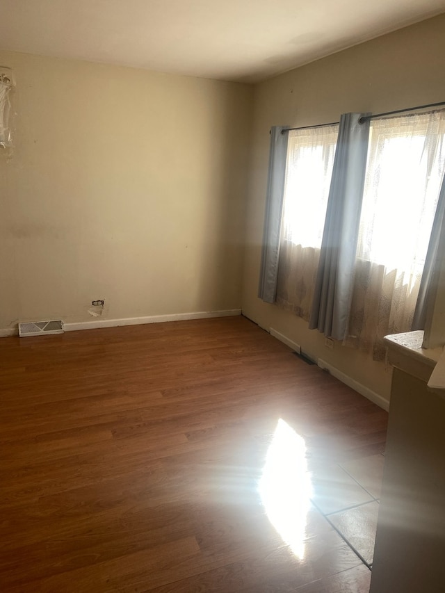 empty room with lofted ceiling, visible vents, baseboards, and wood finished floors