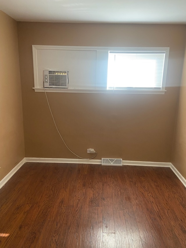 spare room with dark wood finished floors, visible vents, and baseboards