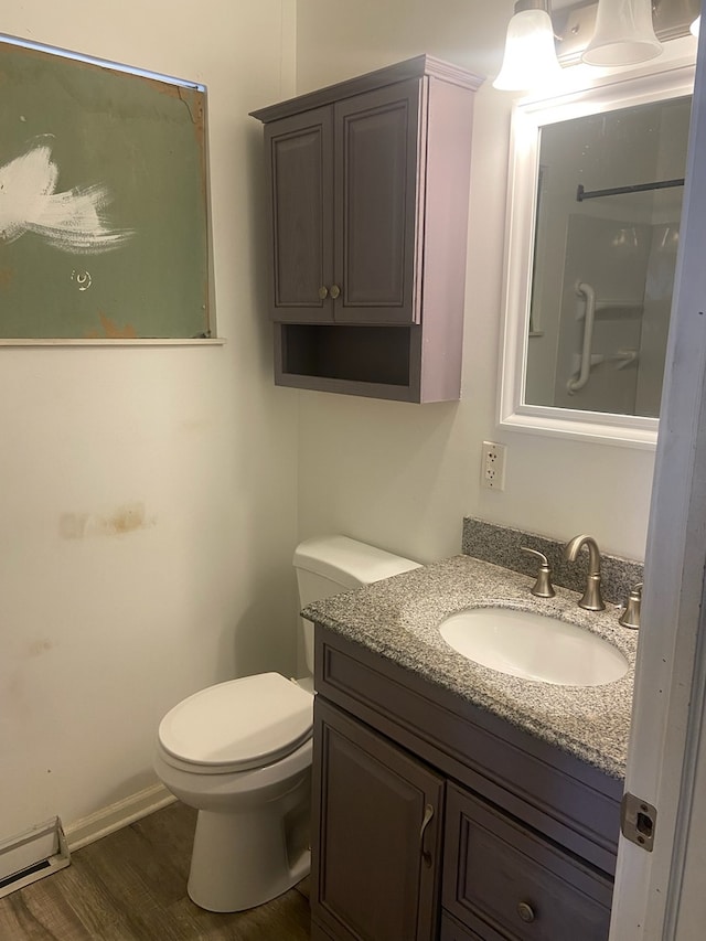 bathroom featuring toilet, a baseboard heating unit, wood finished floors, vanity, and baseboards