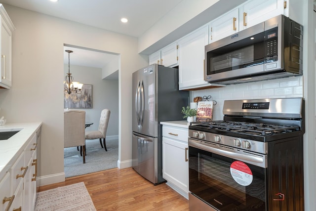 kitchen featuring light stone counters, stainless steel appliances, white cabinets, light wood-type flooring, and backsplash