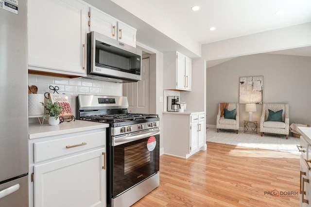 kitchen with appliances with stainless steel finishes, open floor plan, light wood-type flooring, white cabinetry, and backsplash