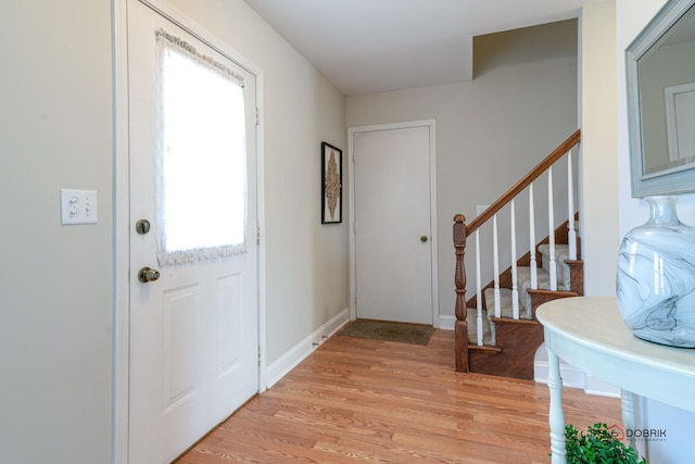 foyer entrance featuring light wood finished floors, baseboards, and stairway