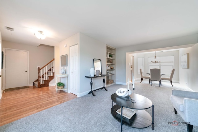 living area with built in shelves, light carpet, visible vents, baseboards, and stairs