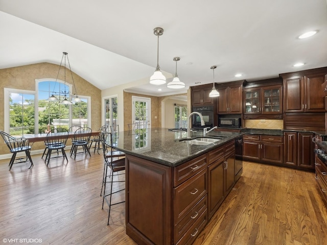 kitchen with vaulted ceiling, black appliances, a breakfast bar area, and wood finished floors