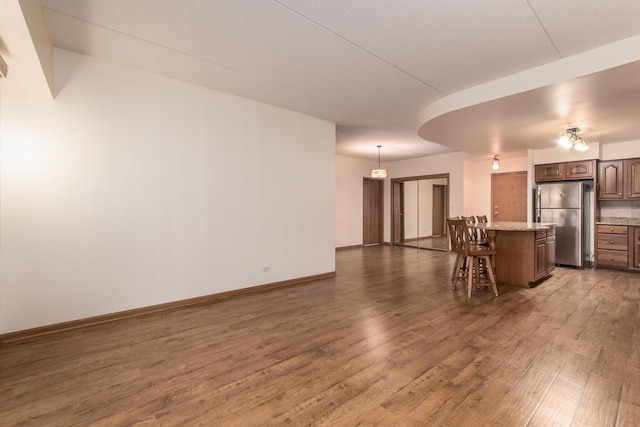 interior space featuring baseboards, open floor plan, a kitchen breakfast bar, wood finished floors, and freestanding refrigerator