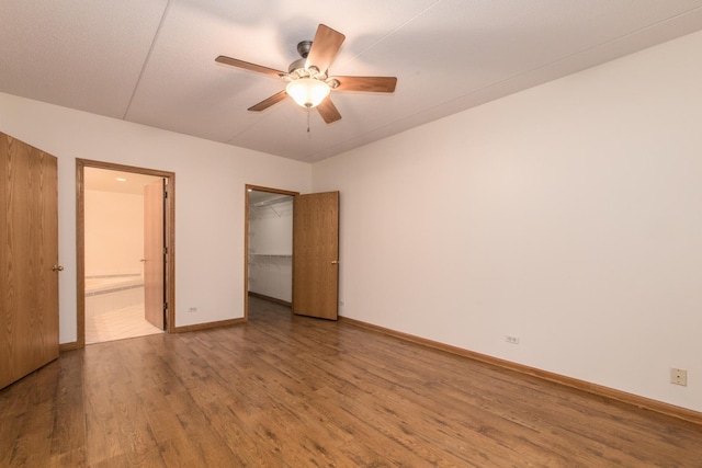 unfurnished bedroom with baseboards, ensuite bath, wood finished floors, a walk in closet, and a closet