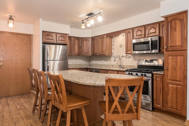 kitchen featuring a center island, backsplash, appliances with stainless steel finishes, light wood-style floors, and light stone countertops