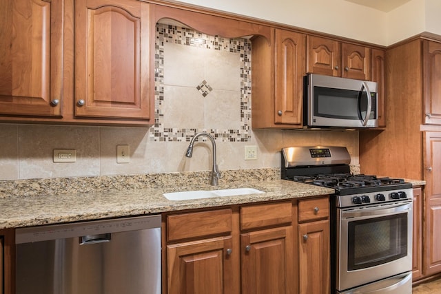 kitchen featuring decorative backsplash, brown cabinetry, light stone countertops, stainless steel appliances, and a sink