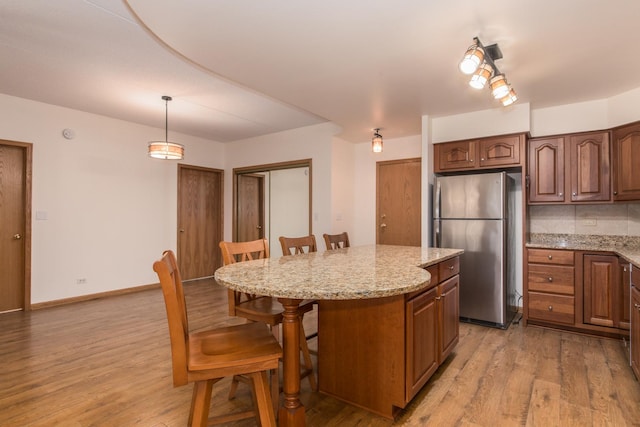 kitchen with a breakfast bar area, light wood-style flooring, a kitchen island, freestanding refrigerator, and light stone countertops