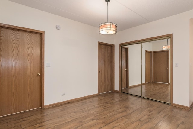 unfurnished bedroom with multiple closets, wood finished floors, and baseboards