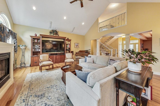 living room with a fireplace, decorative columns, a ceiling fan, wood finished floors, and stairs