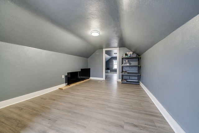 additional living space featuring vaulted ceiling, a textured ceiling, baseboards, and wood finished floors