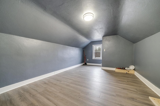 bonus room featuring lofted ceiling, a textured ceiling, baseboards, and wood finished floors