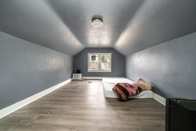 unfurnished bedroom with a textured ceiling, baseboards, vaulted ceiling, and wood finished floors