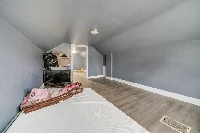 bedroom with lofted ceiling, baseboards, visible vents, and wood finished floors