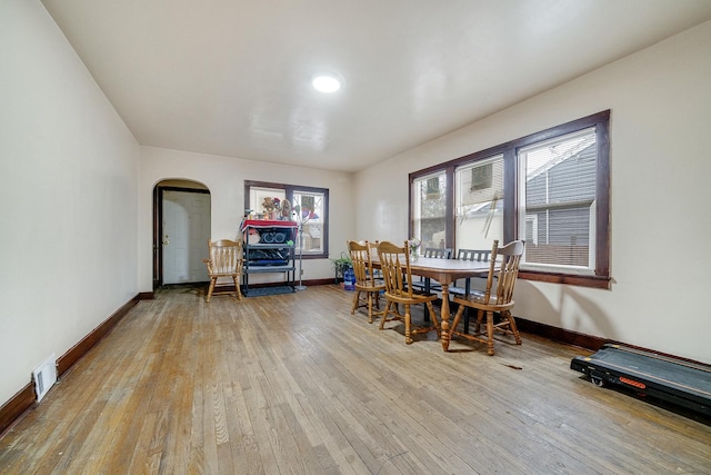 dining space featuring light wood-style floors, arched walkways, visible vents, and baseboards