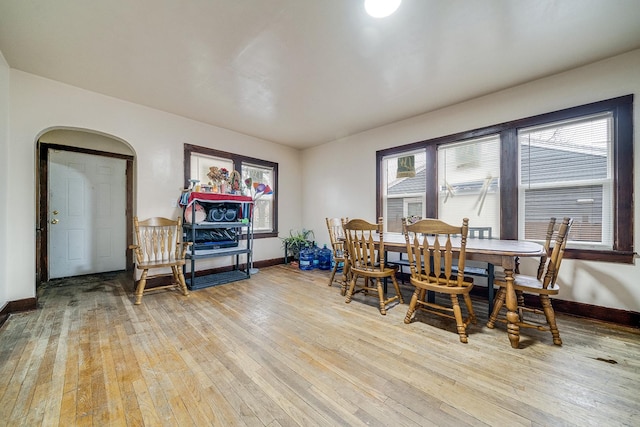 dining area with arched walkways, light wood-style flooring, and baseboards