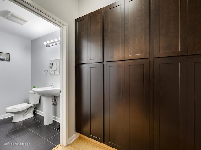 half bath featuring tile patterned flooring, visible vents, toilet, a sink, and baseboards