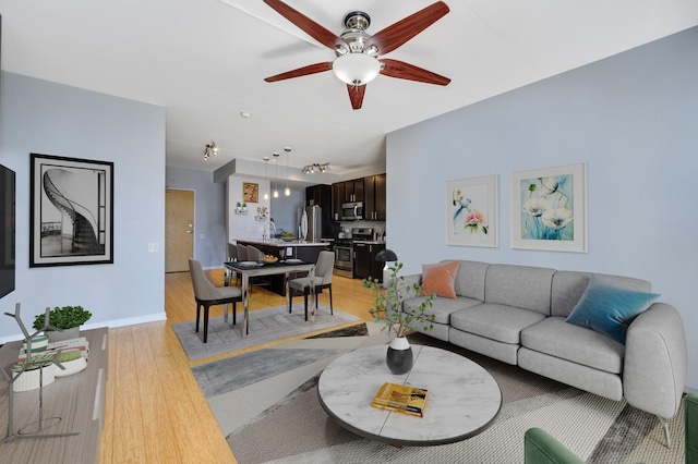 living room featuring light wood finished floors, baseboards, and a ceiling fan