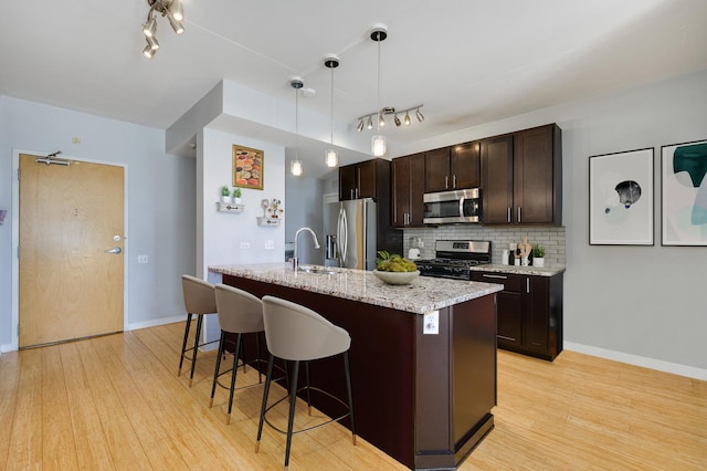 kitchen featuring a kitchen breakfast bar, dark brown cabinets, light wood-type flooring, backsplash, and appliances with stainless steel finishes