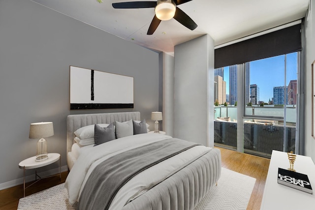 bedroom with ceiling fan, a city view, wood finished floors, and access to exterior