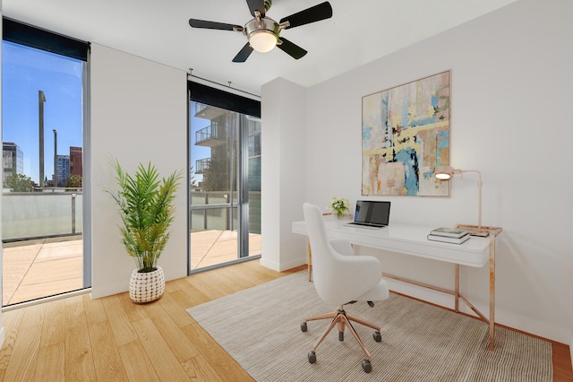 home office featuring ceiling fan, baseboards, wood finished floors, and a wall of windows