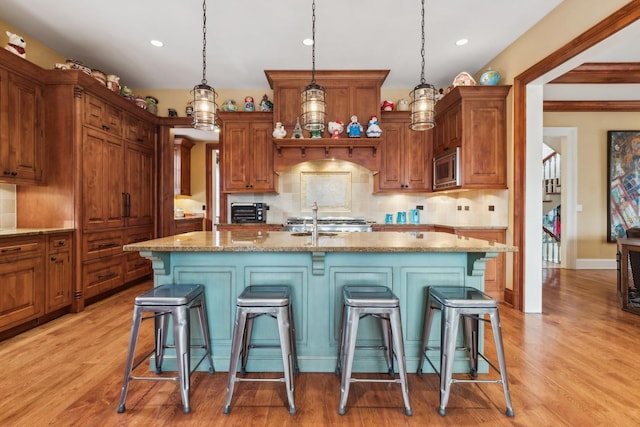 kitchen with an island with sink, stainless steel microwave, a breakfast bar area, and light wood-style floors