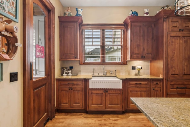 kitchen featuring light wood-style floors, light stone counters, decorative backsplash, and a sink