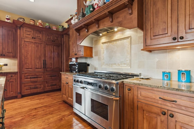 kitchen featuring brown cabinetry, light wood-style flooring, light stone counters, double oven range, and backsplash