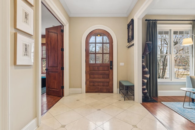 foyer entrance with baseboards, arched walkways, wood finished floors, and ornamental molding