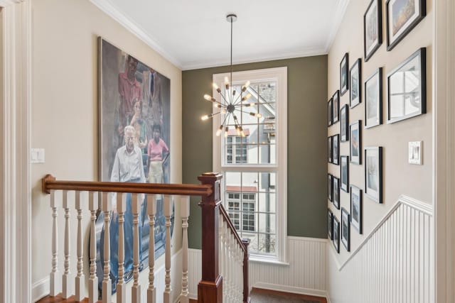 staircase with ornamental molding, a wainscoted wall, plenty of natural light, and a notable chandelier