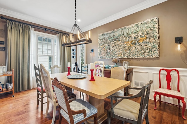 dining space with visible vents, wainscoting, wood finished floors, crown molding, and a decorative wall