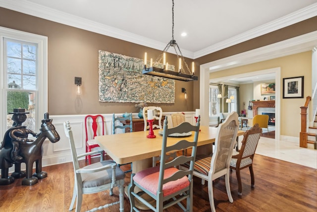 dining room with a wainscoted wall, a lit fireplace, crown molding, and wood finished floors