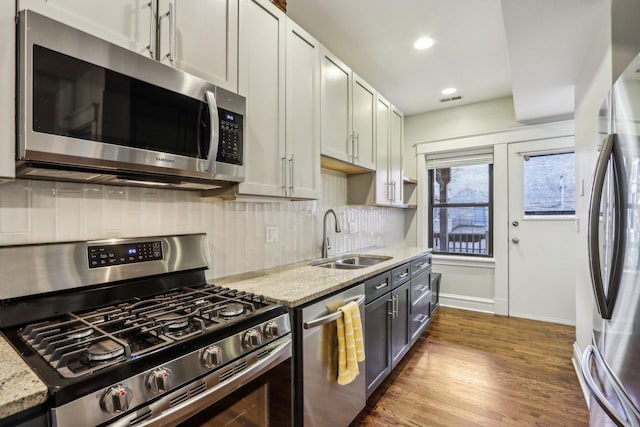 kitchen with tasteful backsplash, light stone counters, wood finished floors, stainless steel appliances, and a sink