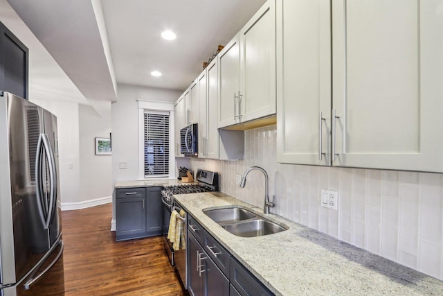 kitchen with stainless steel appliances, dark wood-style flooring, a sink, backsplash, and light stone countertops