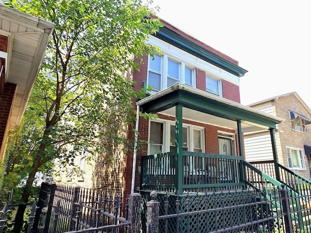 view of front of home with a porch, brick siding, and fence