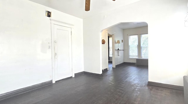 unfurnished room with arched walkways, baseboards, a ceiling fan, and radiator