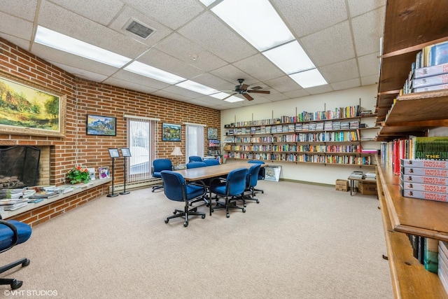 carpeted home office featuring a paneled ceiling, visible vents, ceiling fan, and brick wall