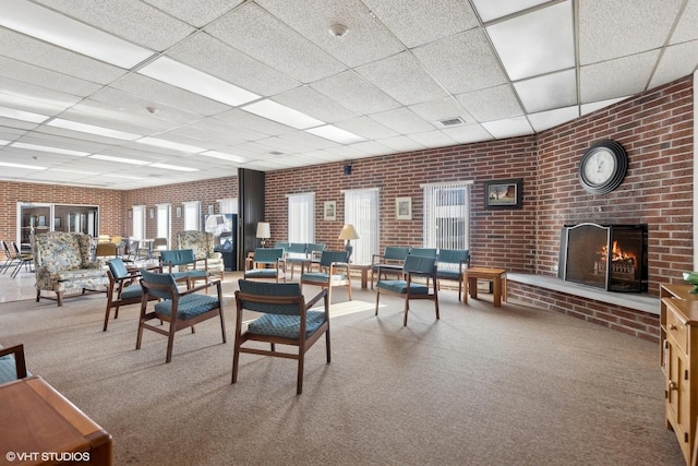 carpeted dining space with brick wall, an outdoor brick fireplace, a drop ceiling, and visible vents