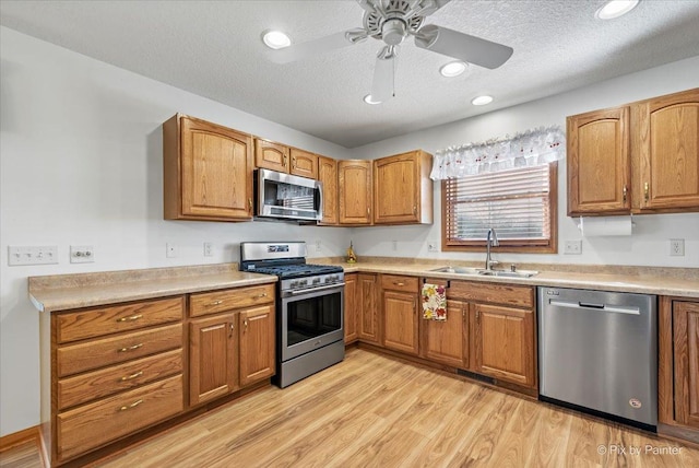 kitchen featuring brown cabinets, light wood-style flooring, appliances with stainless steel finishes, a sink, and a textured ceiling