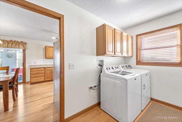 clothes washing area with light wood finished floors, cabinet space, baseboards, washing machine and clothes dryer, and a textured ceiling