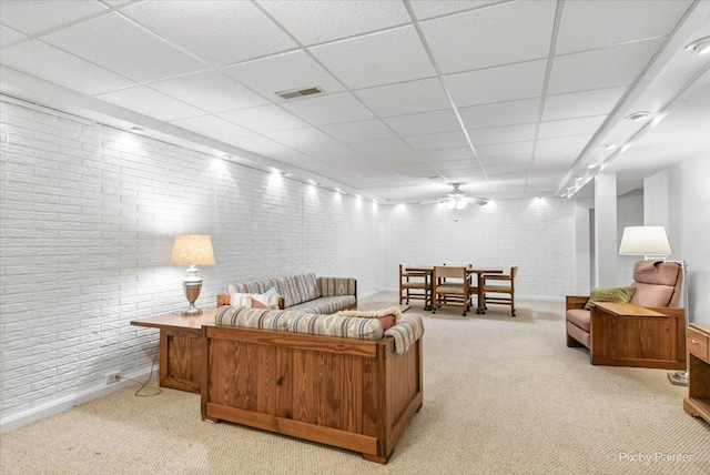 carpeted living area with brick wall, visible vents, and a drop ceiling