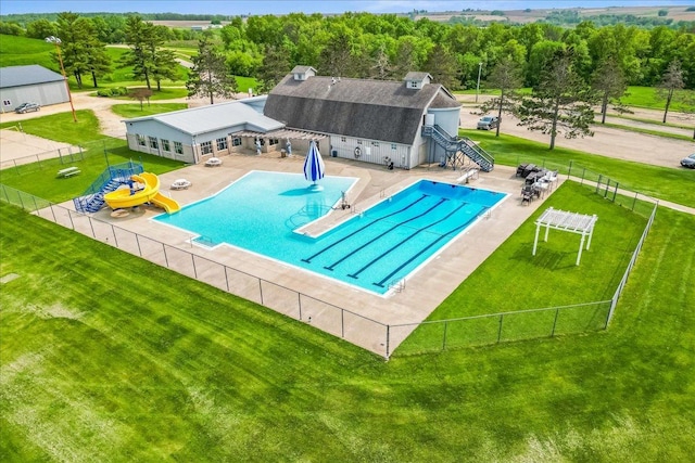 community pool with a patio, a water slide, a lawn, and fence