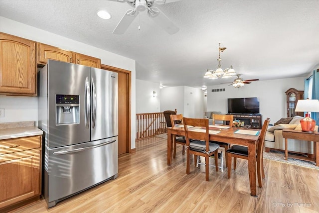 dining space with light wood-style flooring, a textured ceiling, and ceiling fan with notable chandelier