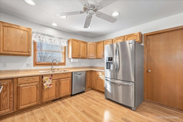 kitchen with a textured ceiling, stainless steel appliances, a sink, and light wood-style floors