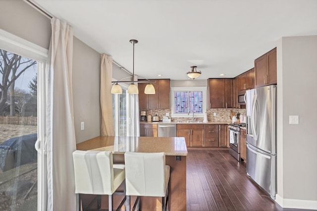 kitchen featuring light stone counters, dark wood-style flooring, backsplash, appliances with stainless steel finishes, and a peninsula