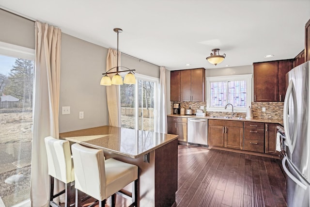 kitchen featuring dark wood-style flooring, a sink, appliances with stainless steel finishes, backsplash, and decorative light fixtures