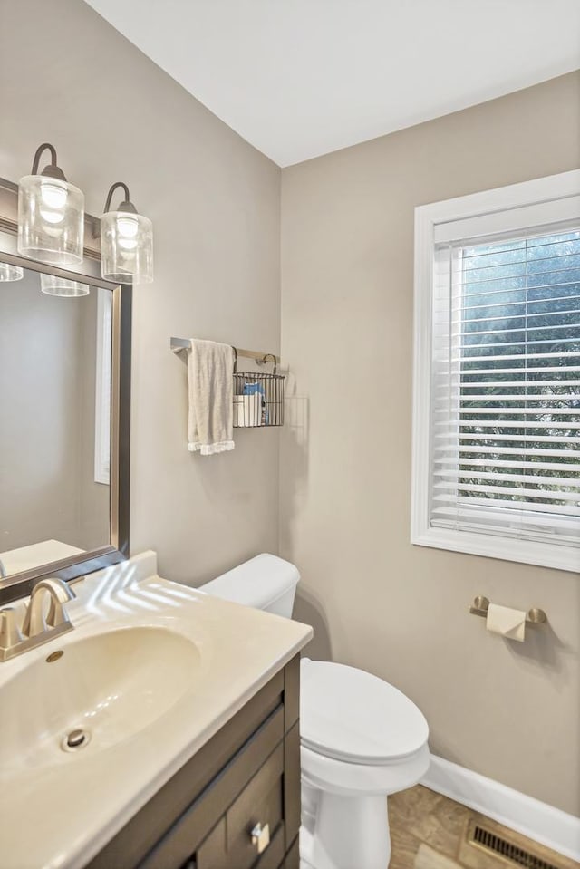 bathroom with toilet, vanity, visible vents, and baseboards